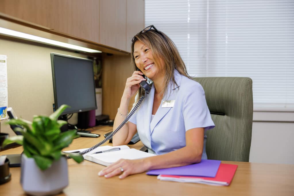 A smiling PARC's receptionist talking on the phone. Independent Senior Living Apartments.
