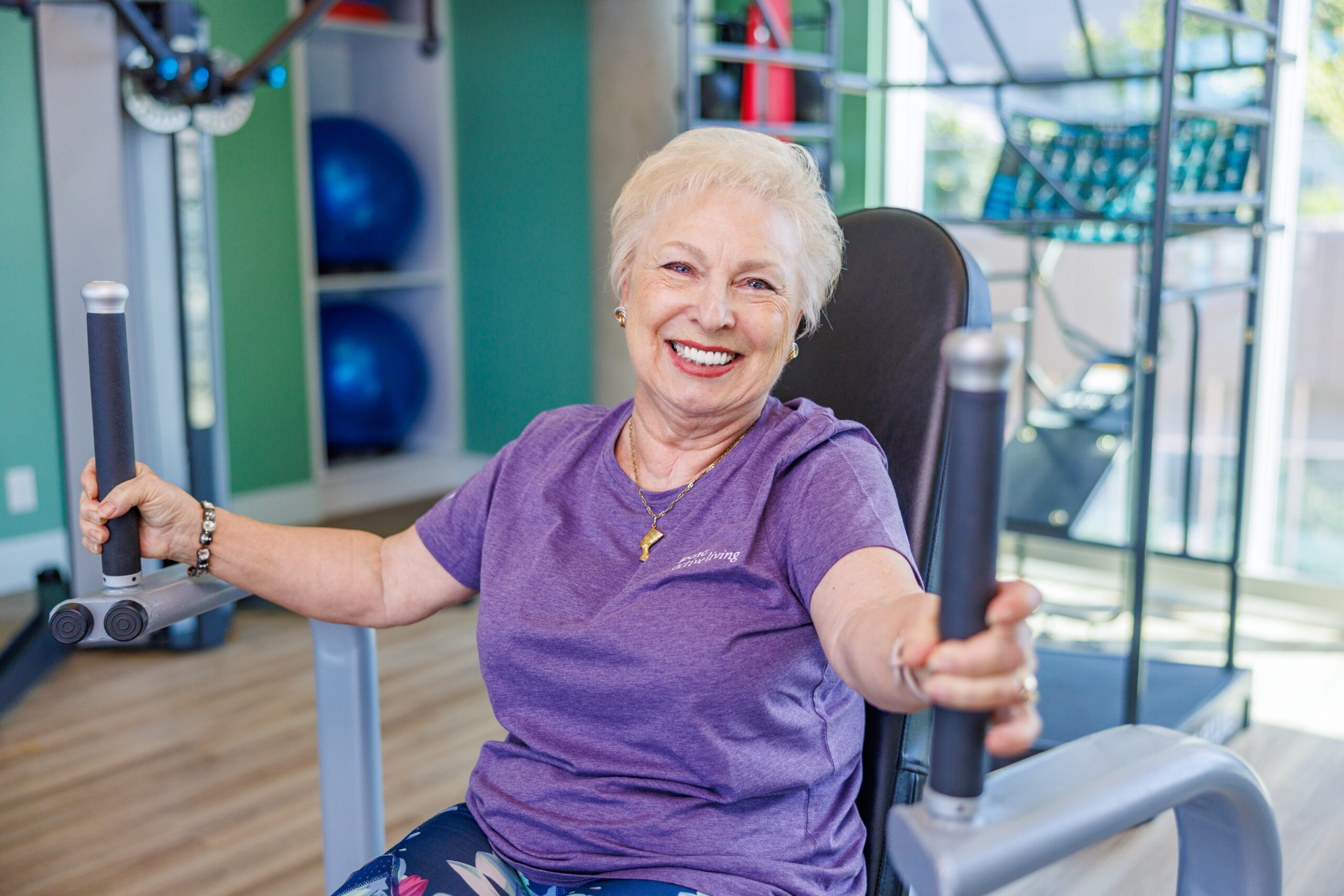 A female senior resident in purple shirt exercising at the gym. Independent Senior Living Community.