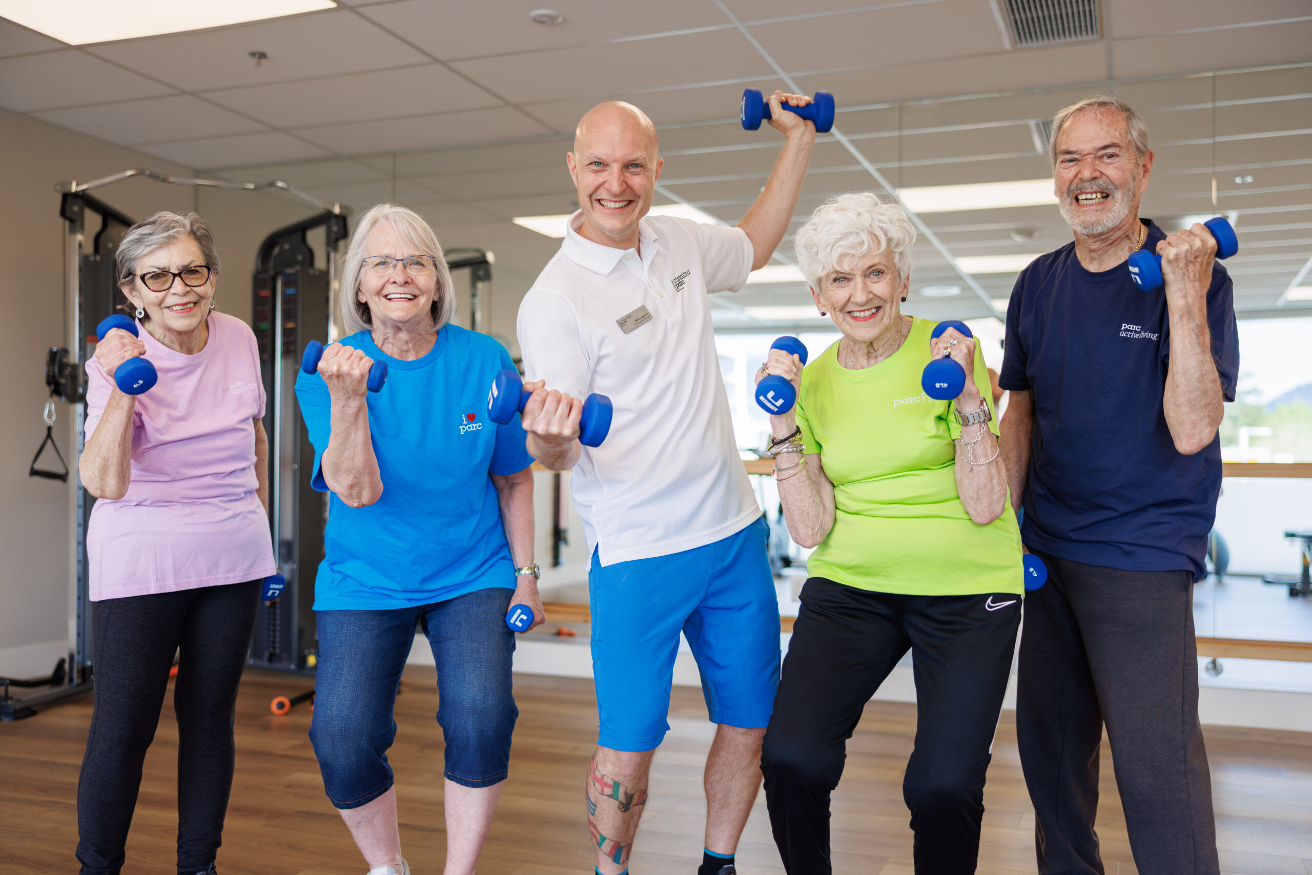 PARC residents at the gym holding weights. A group photo with their fitness trainer. Independent Retirement Community.